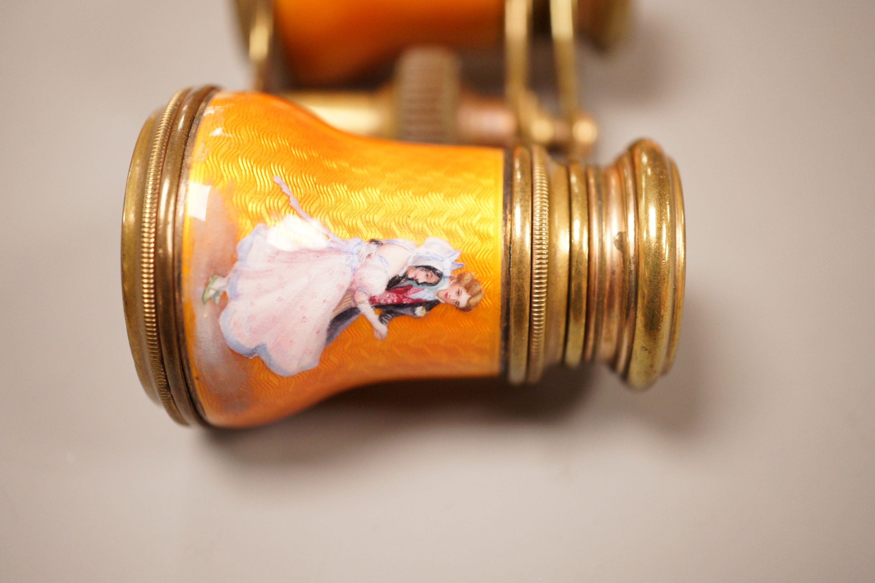 A pair of German orange enamelled opera glasses, inscribed Fabr Emil Busch, Rathenow to the left lens, and E. Petitpierre, BerlinFriedrichstr. to the right lens, 10cm wide